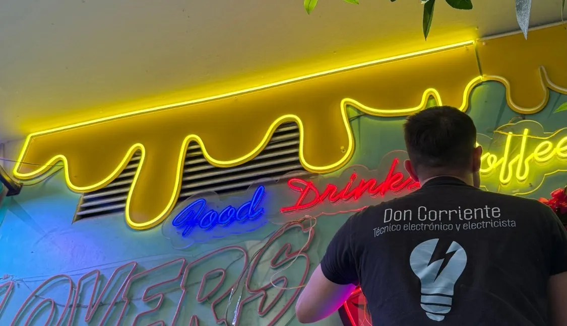 Adrián, from behind in his Don Corriente T-shirt, connecting a café's neon sign