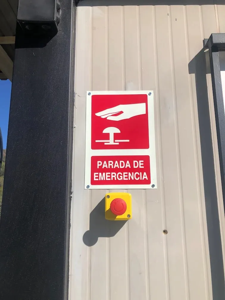 Emergency stop button with its sign, mounted on the wall of an industrial unit